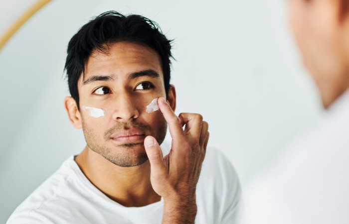 Man applying sunscreen in front of a mirror, morning skincare